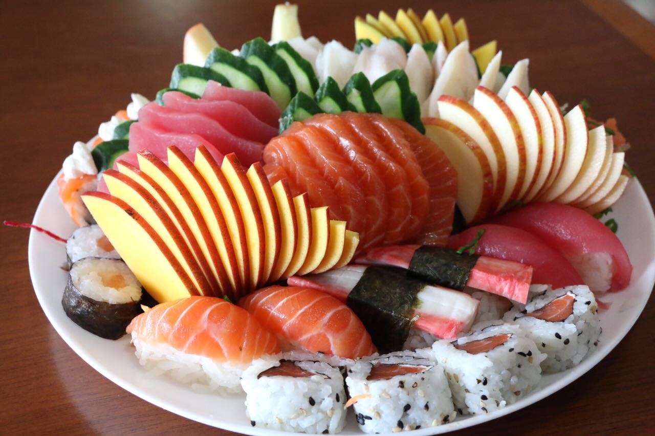 Barca de sushi com sashimis de salmão e atum, uramakis e frutas fatiadas